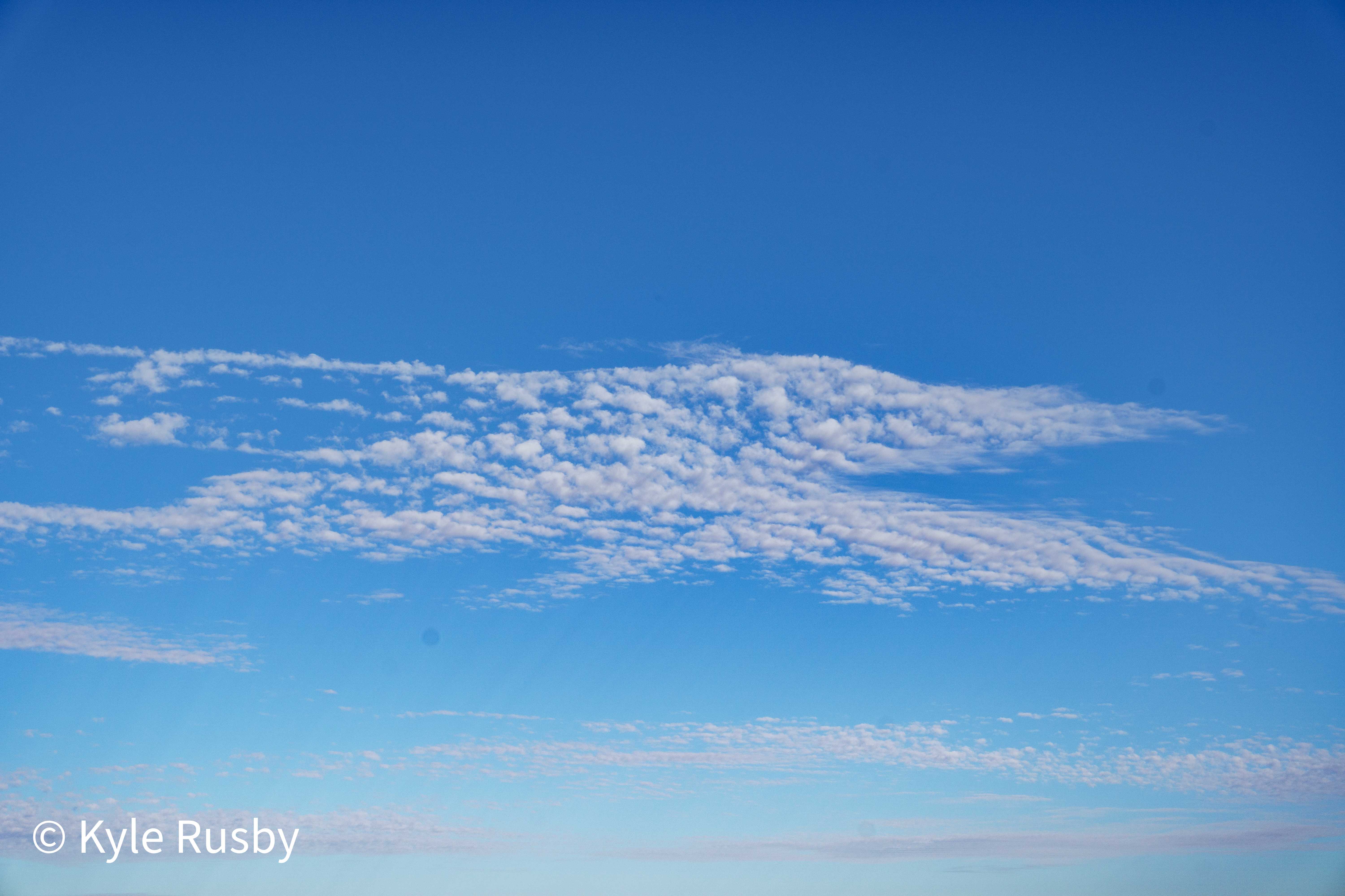 A deep blue sky filled with a drift of small dappled mackerel clouds fading to haze at the horizon